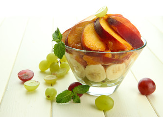 Tasty fruit salad in glass bowl, on white wooden table