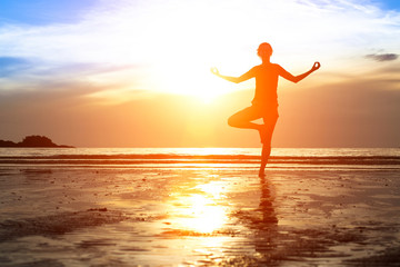 Fototapeta na wymiar Silhouette woman practicing yoga on the beach at sunset