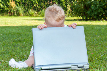 Baby sitting with laptop in a meadow