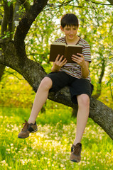 Handsome teenage boy sitting on the tree and reading old book