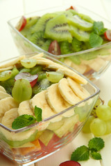 Tasty fruit salad in glass bowls, on white wooden table