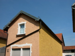 Kleine Häuschen mit spitzem Giebel und Fassaden in Beige und Naturfarben vor blauem Himmel im...