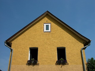 Wohnhaus mit spitzem Giebel und Fassade in Beige und Naturfarben vor blauem Himmel im Sonnenschein...