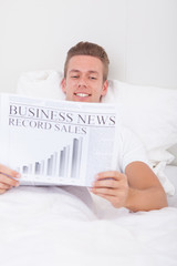 Young Man Lying On Bed Reading Newspaper