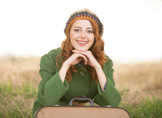 Redhead girl with suitcase sitting at autumn grass