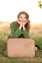 Redhead girl with suitcase sitting at autumn grass