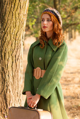 Redhead girl with suitcase at tree's alley.