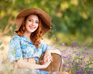 Redhead girl with suitcase sitting at autumn grass