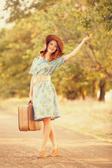 Redhead girl with suitcase at tree's alley.