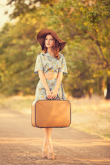 Redhead girl with suitcase at tree's alley.