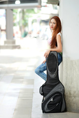 Young beautiful woman posing outdoor with her guitar gig bag