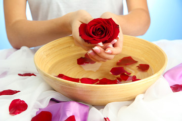 woman hands with wooden bowl of water with petals,