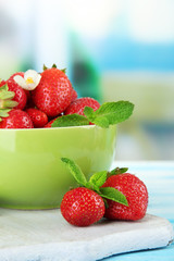 Ripe sweet strawberries in green bowl on blue wooden table