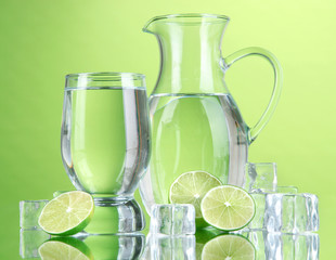 Glass pitcher of water and glass on green background
