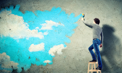 Young man drawing a cloudy blue sky