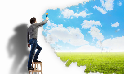 Young man drawing a cloudy blue sky