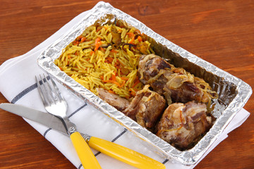 Food in box of foil on napkin on wooden background