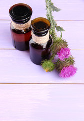 Medicine bottles with thistle flowers on wooden background