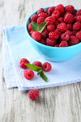 Ripe sweet raspberries in bowl on wooden background