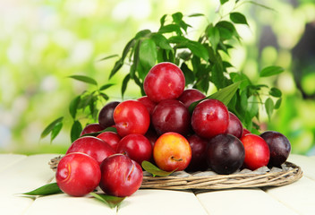 Ripe plums in basket on wooden table on natural background