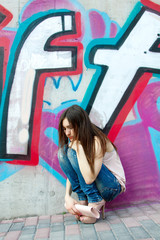 portrait of beautiful fashion girl sitting near wall with abstra