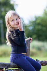 Obraz premium Posing small Caucasian girl sitting on village fence at summer