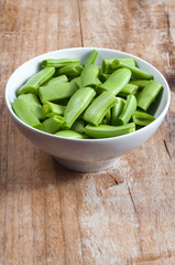 Raw green beans in a bowl, on a wooden table