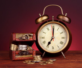 Antique clock and coins on wooden table on dark color