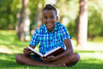 Outdoor portrait of student black boy reading a book - African p