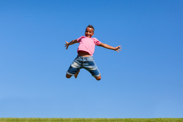 Outdoor portrait of a cute teenage black boy jumping over a blue
