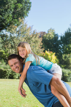 Daughter getting piggy back from dad smiling at camera