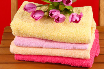Obraz na płótnie Canvas Ręczniki i kwiaty na drewnianym krześle na czerwonym tle