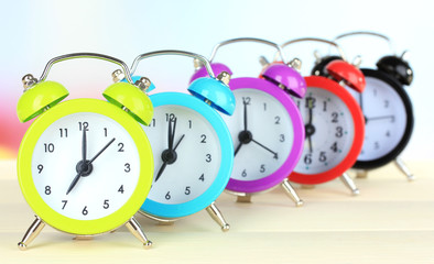 Colorful alarm clocks on table on light background