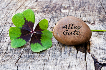 vierblättriges Kleeblatt mit Stein auf Holz, Alles Gute