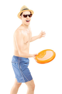 Smiling guy in swimming shorts throwing frizbee