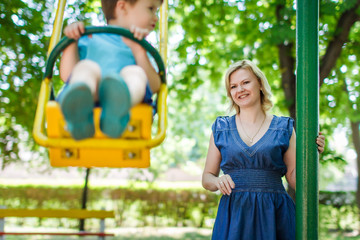 Obraz premium Young caucasian mother with swinging son at playground