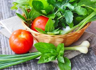 Fresh vegetables and greenery are in a basket on a wooden