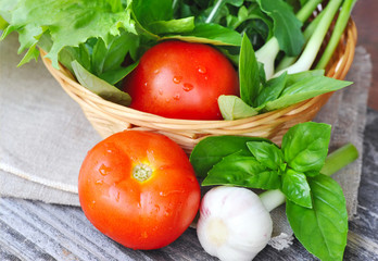 Fresh vegetables and greenery are in a basket on a wooden