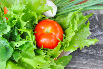 Fresh vegetables and greenery are in a basket on a wooden