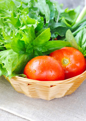 Fresh vegetables and greenery are in a basket on sackcloth