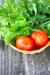 Fresh vegetables and greenery are in a basket on a wooden