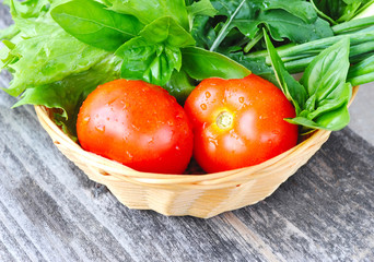 Fresh vegetables and greenery are in a basket on a wooden