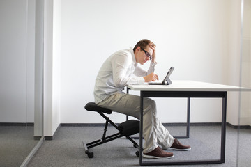 bad sitting posture at workstation. man on kneeling chair - obrazy, fototapety, plakaty