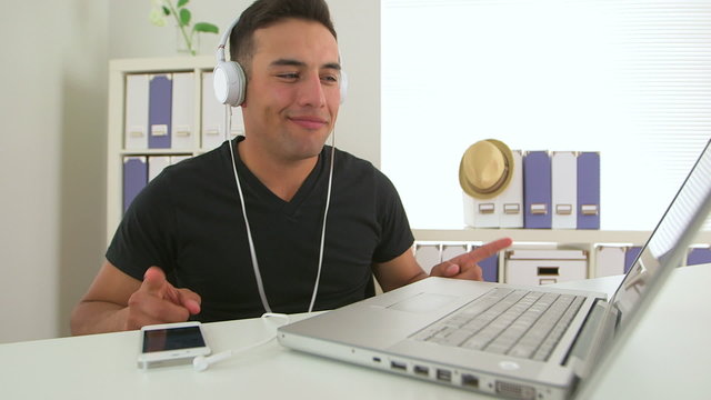 Hispanic business man listening to music in office at laptop