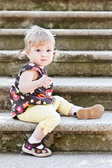 Fototapeta premium Little cute girl in sitting on the stairs with stone steps