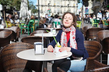 Young happy woman eats ice cream at outdoor cafe on sunny day.