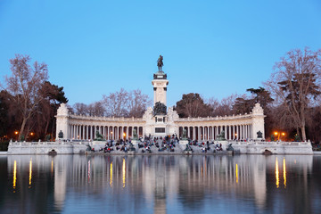 Fototapeta na wymiar Tourists sit near monument to Alfonso XII at pond in Retiro Park