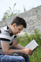 Young brunet man in jeans intently reads book outdoor at summer