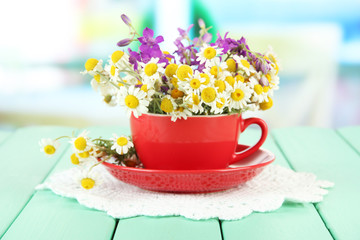Bouquet of chamomile flowers in cup, on bright background