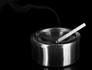 Metal ashtray and cigarette on black background